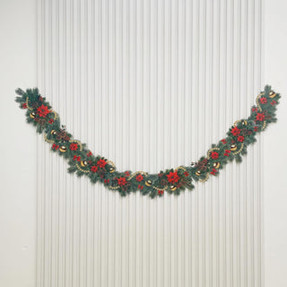Christmas garland with pine leaves, red poinsettias, and gold ornaments on a wall