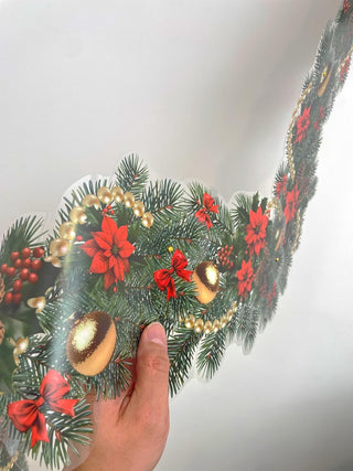 Hand adjusting Christmas garland with pine, red poinsettias, and gold ornament baubles