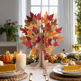Tree centerpiece with layered red, orange, and gold maple leaves on pale wooden stand