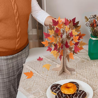 Autumn leaf tree centerpiece on table with layered red, orange, and beige leaves on wooden stand