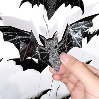 Black geometric glitter bat ornament held by hand on hanging string