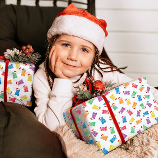 Child wearing Santa hat holding candy bear printed gift box wrapped in white paper