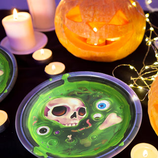 Round Halloween party plate with green skull face graphic and purple rim on table