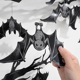 Black bat hanging banner with silver-speckled wings and bat face center, held by hand