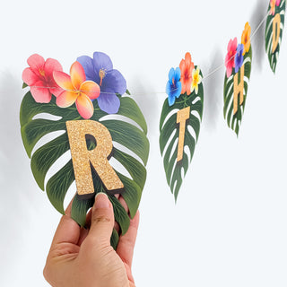 Gold glitter letter R on leaf pennant with flowers and toucan topper, held by hand
