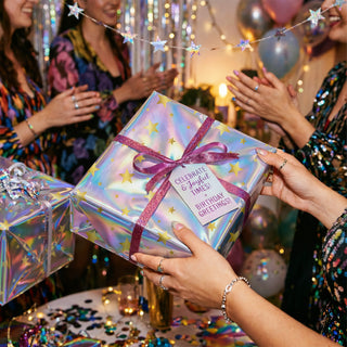 Iridescent star gift wrap with gold stars, held gift box with glittery bow