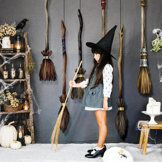 Flying broomstick garland with assorted brush brooms hanging behind a witch holding a broom