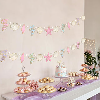 Pastel undersea banner garland with starfish, shells, and seahorse above desserts