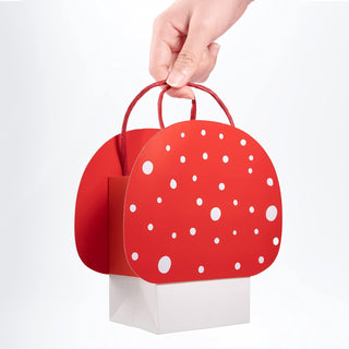 Red polka-dot mushroom gift bag held by a hand, with white dots and red handles