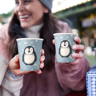 Blue paper cups with penguin print held in hands at outdoor birthday party