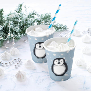 Blue penguin paper cups with white tissue and striped straws on winter table