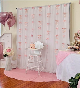Pink satin bow garland with pearl bead strings hanging across a sheer party curtain