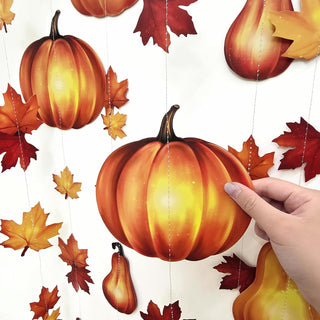 Hand adjusting pumpkin and leaf garland string with hanging gourds