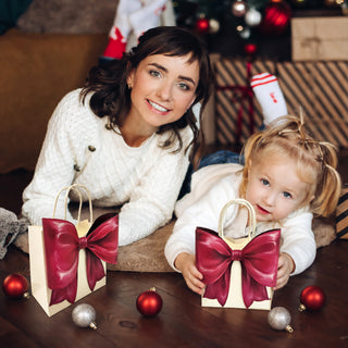 Small cream gift bag with burgundy bow and rope handles, held by child