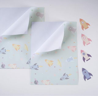 Stacked rocket-themed wrapping paper sheets with star and planet pattern, pastel colors