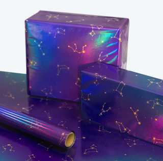 Galaxy constellation foil gift wrap stacked with roll end, purple galaxy and gold star symbols