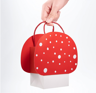 Red mushroom party favor bag with white polka dots and red loop handles, held up