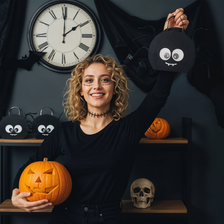 Black spider-shaped gift bag with cartoon eyes, loop handle and legs, held in hand