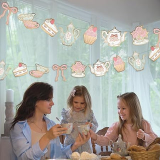 Tea party banner hung above table with pastel teapot, teacup, bow, and cupcake decorations