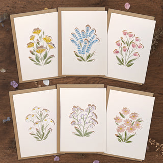 Wildflower greeting card set with six botanical designs on envelopes, flat lay on wood