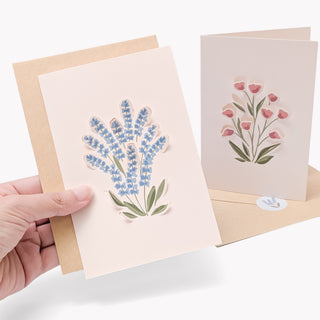 Two wildflower greeting cards with envelopes, hands holding blue and pink floral designs