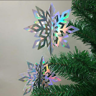 Holographic iridescent 3D snowflake hanging ornament next to green tree tips
