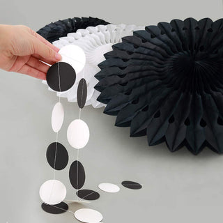 Hand holding a black-and-white dot garland strand next to a large paper rosette
