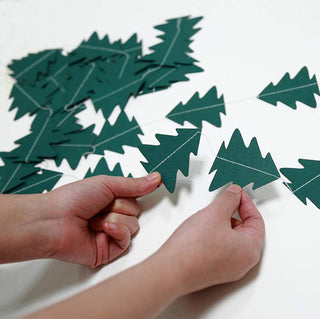 Hands attaching dark green tree cutout garland to wall string
