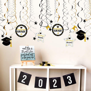 Gold and black graduation hanging swirls at a grad party, featuring paper Congrats Grad medallions, stars, and caps